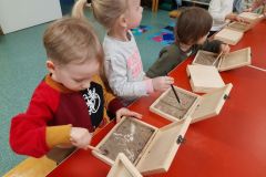 Dzieci z grupy I szukają w pudełkach z piaskiem szkielety dinozaurów