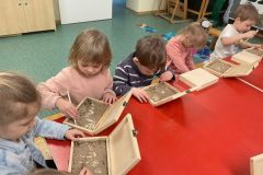 Dzieci z grupy II szukają w pudełkach z piaskiem szkielety dinozaurów
