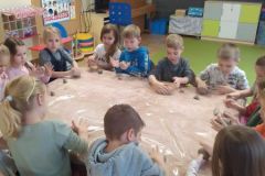 Przedszkolaki z grupy V siedzą przy stolikach w swojej sali  i lepią z gliny